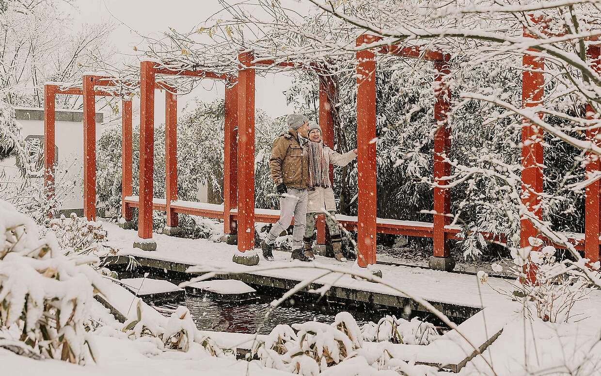 Ein Paar geht im verschneiten Chinesischen Garten unter der roten Pergola spazieren