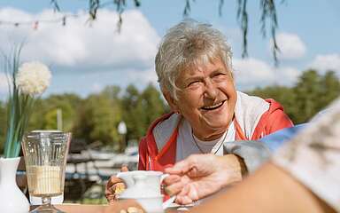 Eine ältere Dame sitzt am Tisch bei Kaffee und Kuchen