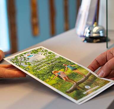 Mitarbeiter der Touristinfo übergibt Infobroschüre an Kunde